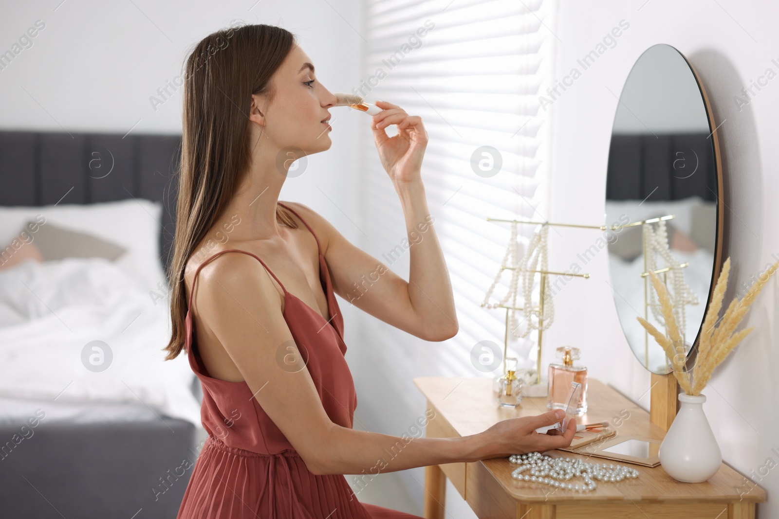 Photo of Getting ready. Young woman applying makeup near mirror at vanity indoors