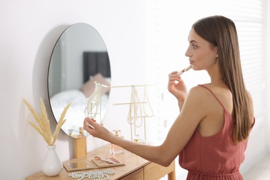 Photo of Getting ready. Young woman applying makeup near mirror at vanity indoors