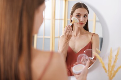 Photo of Getting ready. Young woman applying makeup near mirror at vanity indoors
