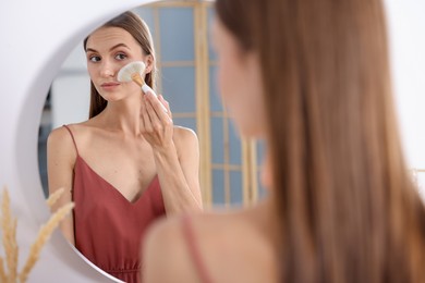 Photo of Getting ready. Young woman applying makeup near mirror at vanity indoors