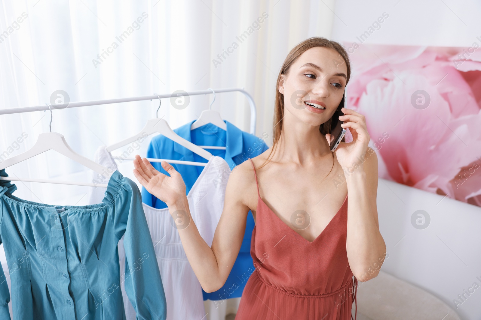 Photo of Getting ready. Young woman talking on phone and choosing clothes at home
