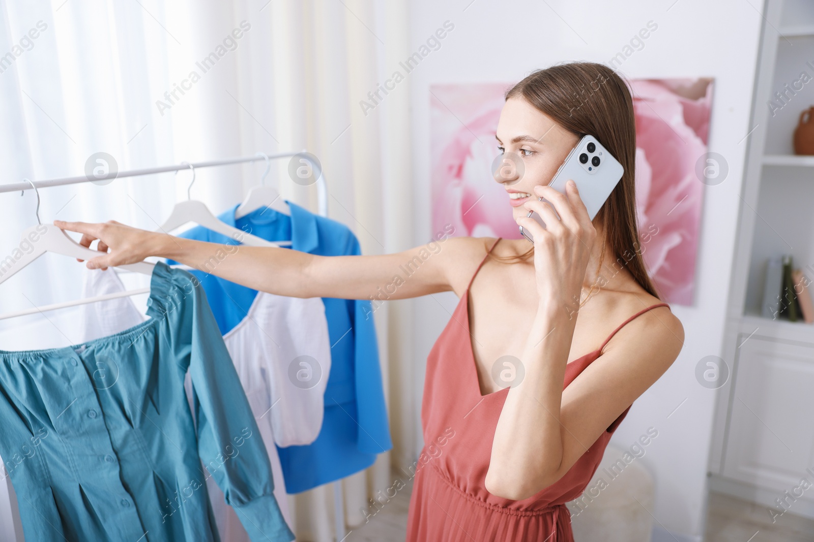 Photo of Getting ready. Young woman talking on phone and choosing clothes at home