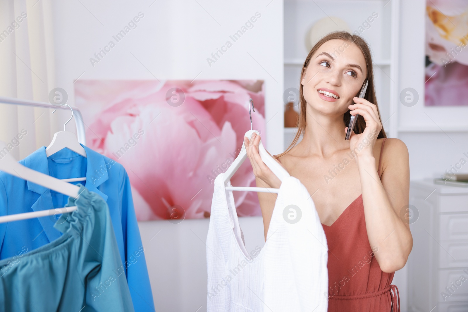 Photo of Getting ready. Young woman talking on phone and choosing clothes at home