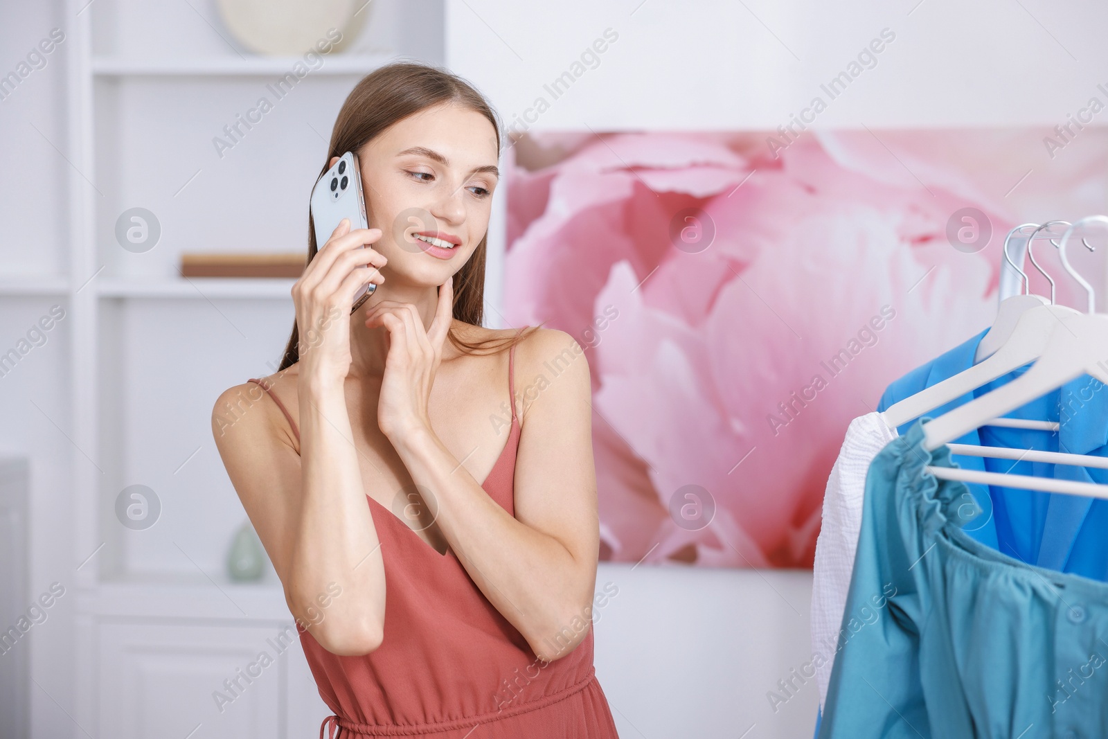 Photo of Getting ready. Young woman talking on phone and choosing clothes at home