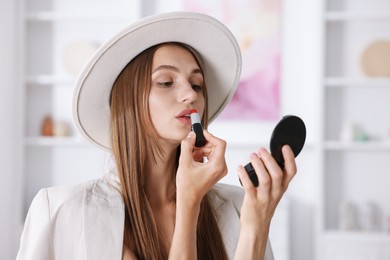 Photo of Getting ready. Young woman in stylish clothes applying lipstick at home