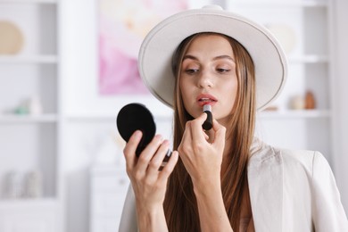 Photo of Getting ready. Young woman in stylish clothes applying lipstick at home