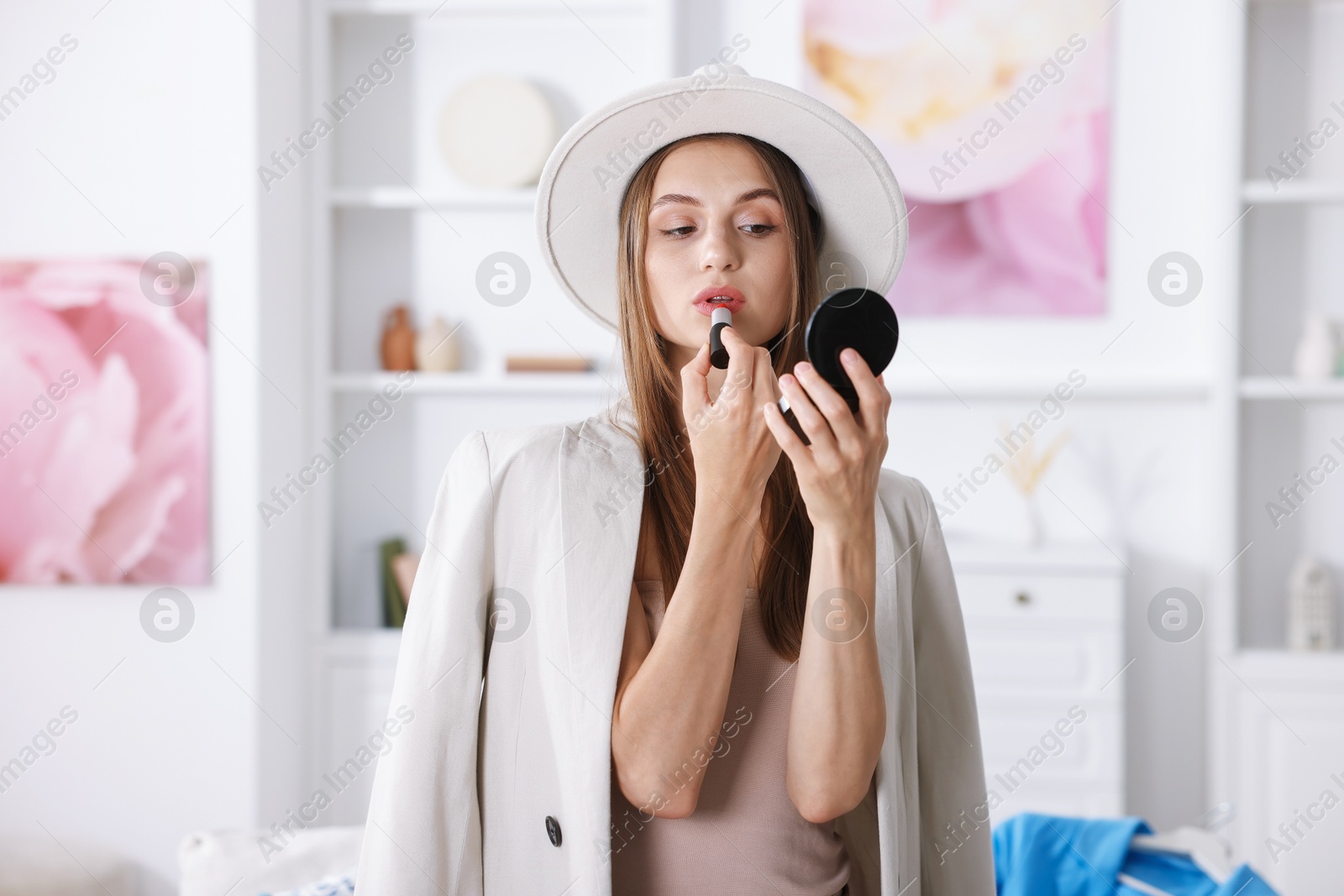 Photo of Getting ready. Young woman in stylish clothes applying lipstick at home