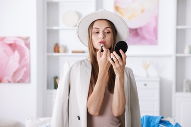 Photo of Getting ready. Young woman in stylish clothes applying lipstick at home