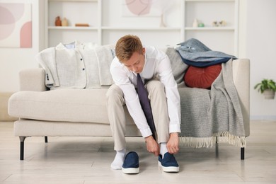 Photo of Getting ready. Young man putting on stylish shoes at home