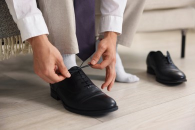 Photo of Getting ready. Young man putting on stylish shoes at home, closeup