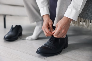 Photo of Getting ready. Young man putting on stylish shoes at home, closeup
