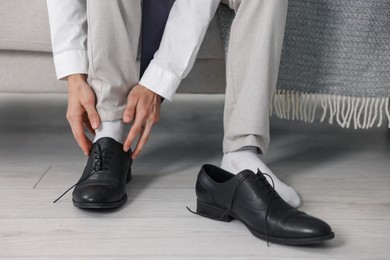 Photo of Getting ready. Young man putting on stylish shoes at home, closeup