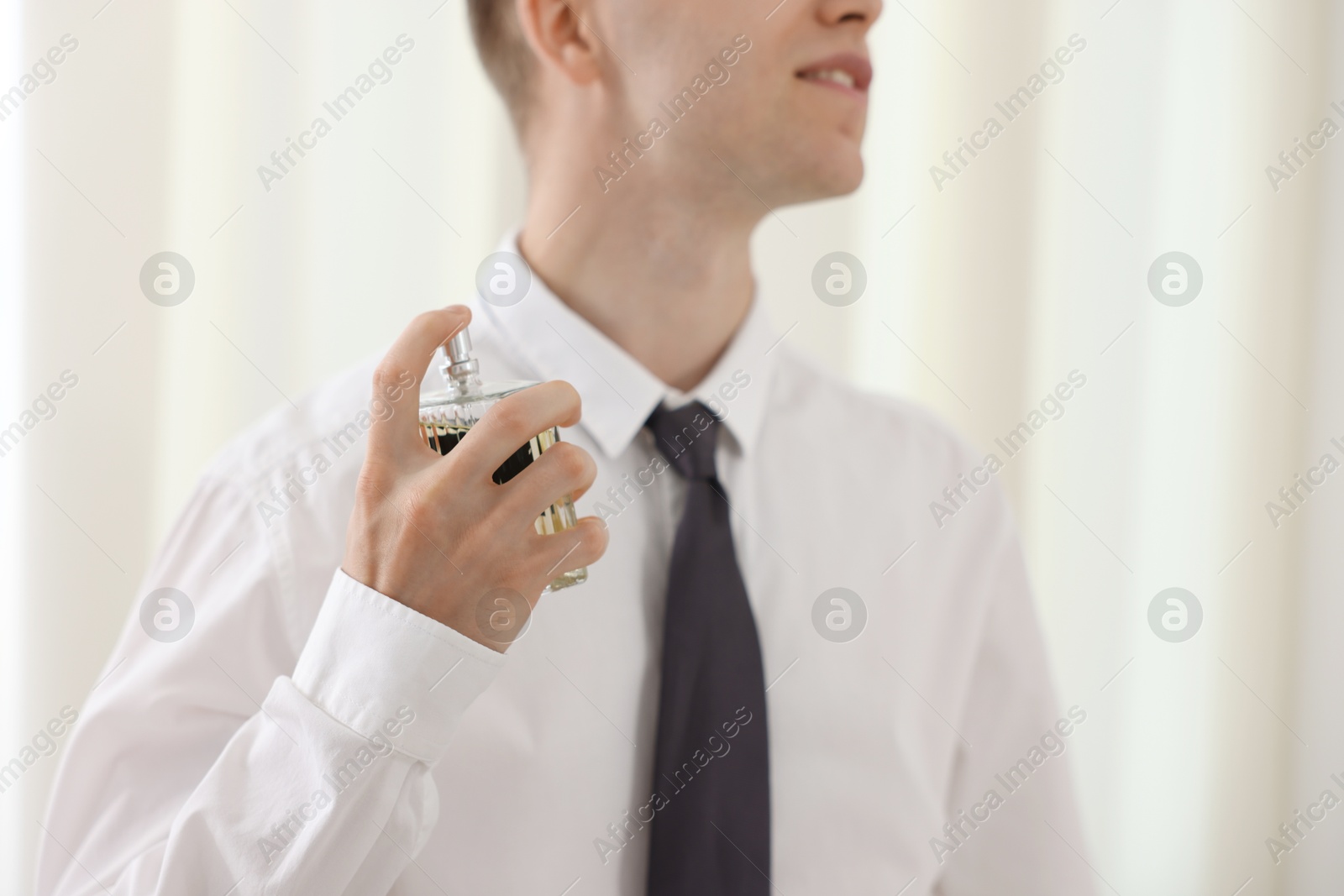Photo of Getting ready. Young man applying perfume at home, closeup