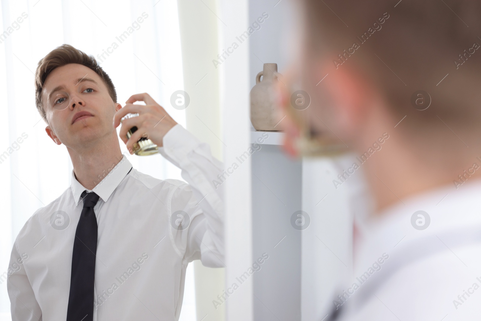 Photo of Getting ready. Young man applying perfume near mirror at home