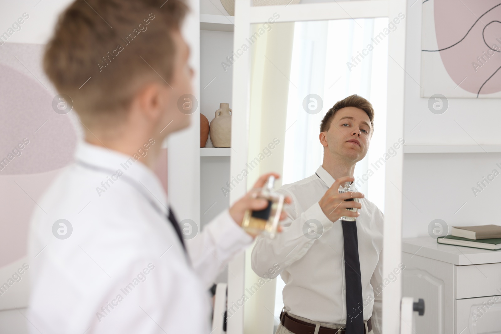 Photo of Getting ready. Young man applying perfume near mirror at home