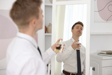 Photo of Getting ready. Young man applying perfume near mirror at home