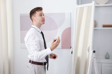 Photo of Getting ready. Young man applying perfume near mirror at home