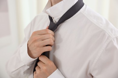Photo of Getting ready. Young man tying stylish necktie at home, closeup