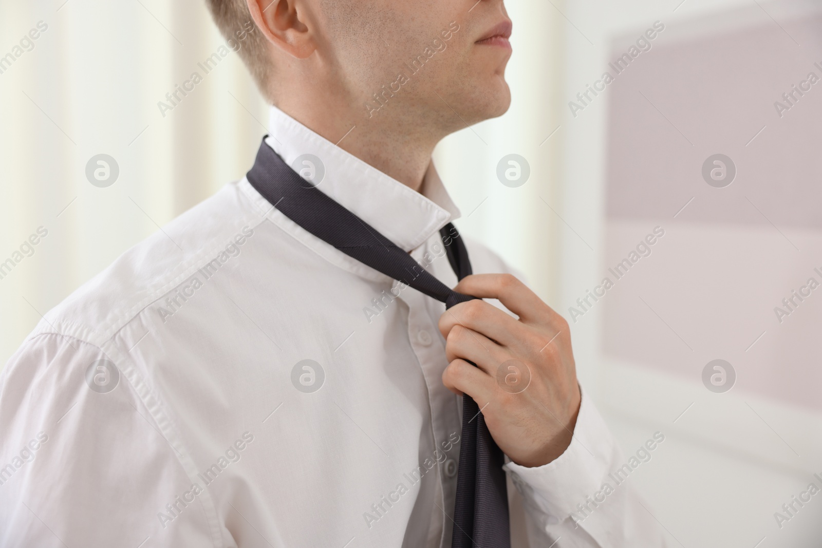 Photo of Getting ready. Young man tying stylish necktie at home, closeup