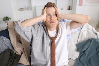 Photo of Getting ready. Stressed young man choosing clothes at home