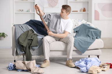 Photo of Getting ready. Sad young man choosing clothes at home