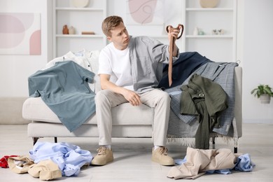 Photo of Getting ready. Sad young man choosing clothes at home