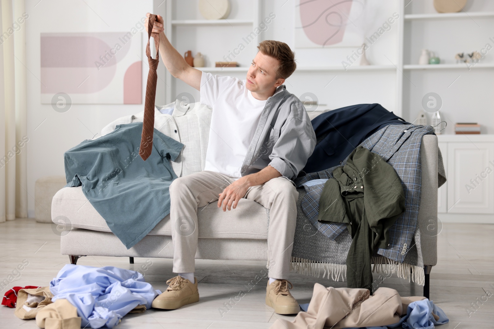 Photo of Getting ready. Sad young man choosing clothes at home