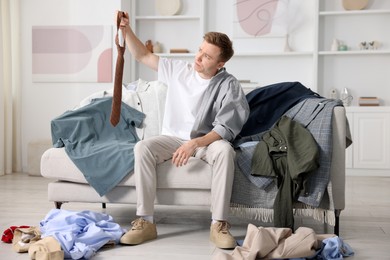 Photo of Getting ready. Sad young man choosing clothes at home