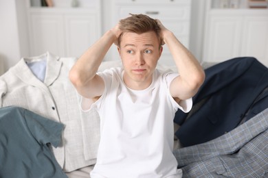 Photo of Getting ready. Stressed young man choosing clothes at home