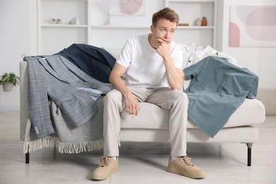 Photo of Getting ready. Sad young man choosing clothes at home