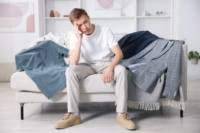 Photo of Getting ready. Sad young man choosing clothes at home