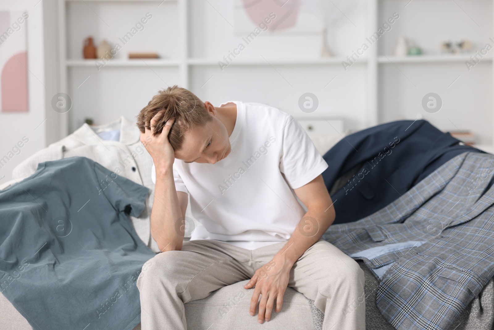 Photo of Getting ready. Sad young man choosing clothes at home