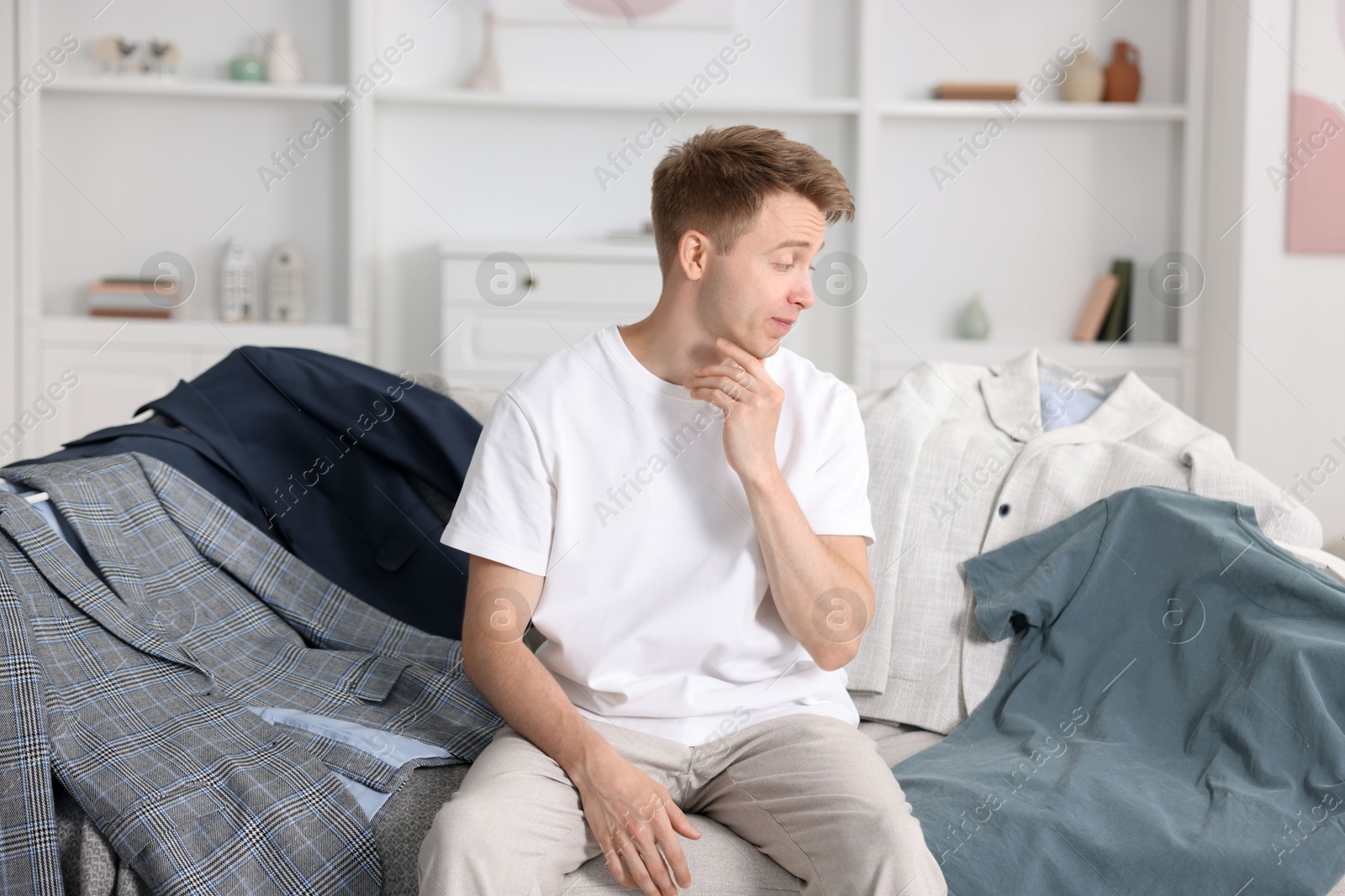 Photo of Getting ready. Sad young man choosing clothes at home