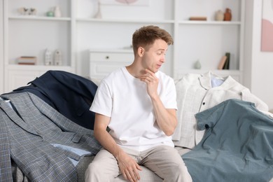 Photo of Getting ready. Sad young man choosing clothes at home