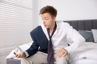 Photo of Shocked young man with alarm clock getting ready at home