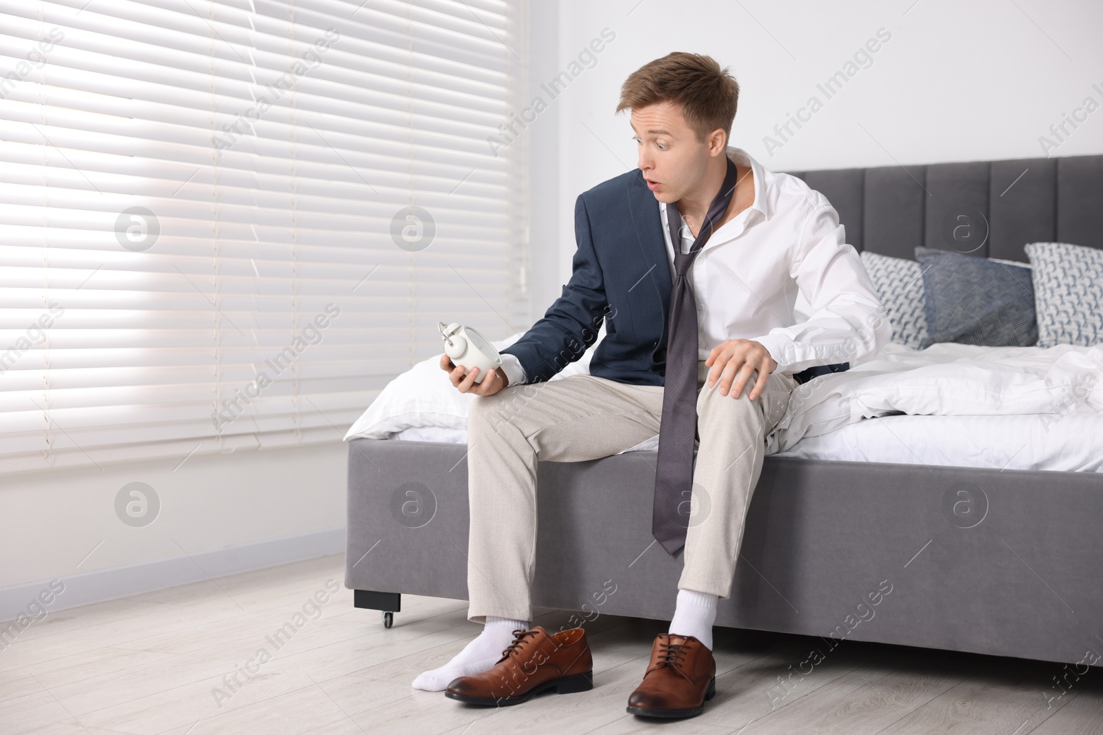 Photo of Shocked young man with alarm clock getting ready at home