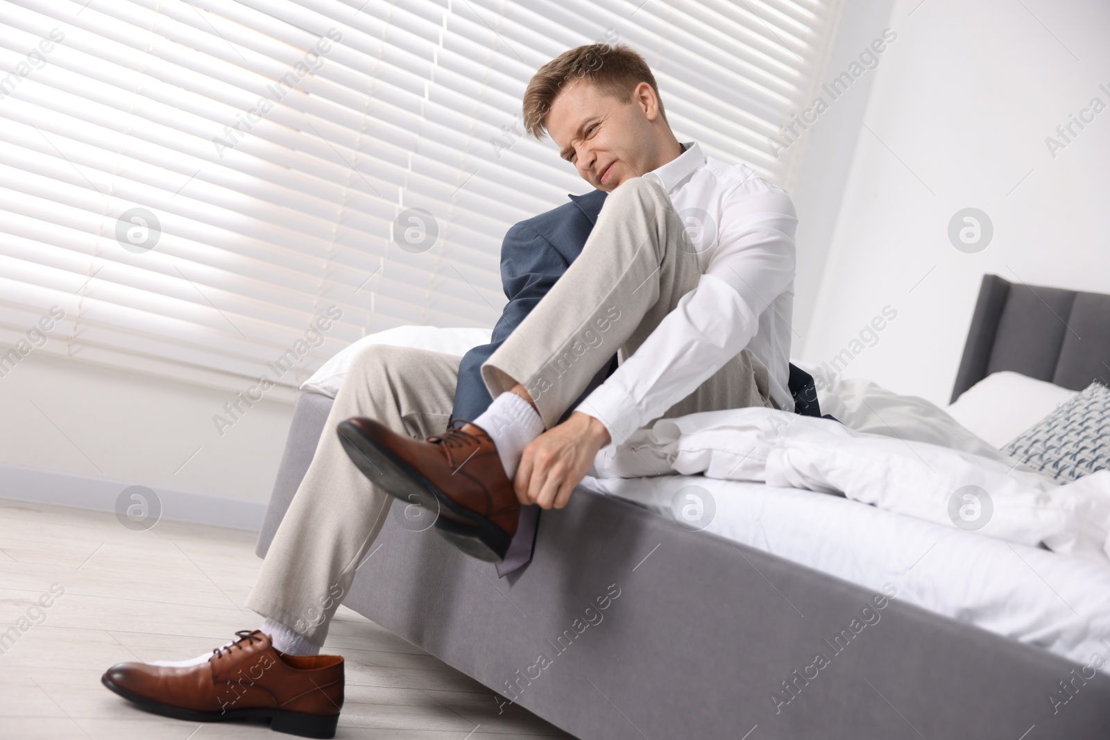Photo of Getting ready. Young man putting on stylish shoes at home