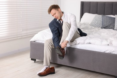 Photo of Getting ready. Young man putting on stylish shoes at home