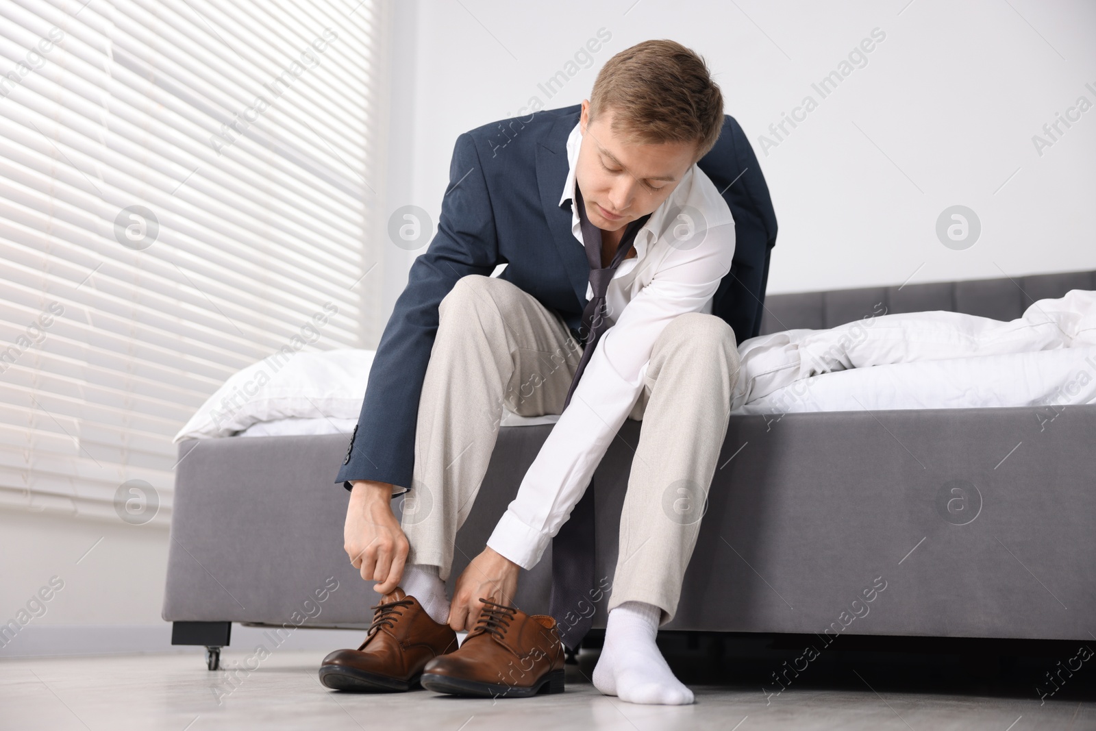 Photo of Getting ready. Young man putting on stylish shoes at home