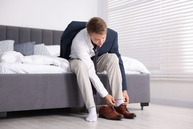 Photo of Getting ready. Young man putting on stylish shoes at home