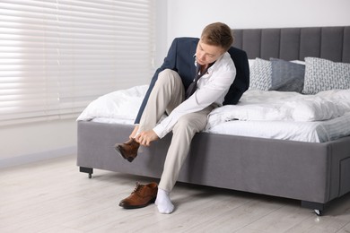 Photo of Getting ready. Young man putting on stylish shoes at home