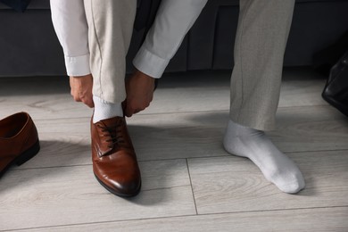 Photo of Getting ready. Young man putting on stylish shoes at home, closeup