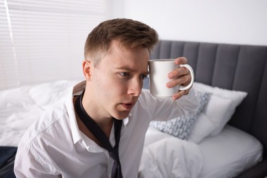 Photo of Sad young man with cup of coffee getting ready at home
