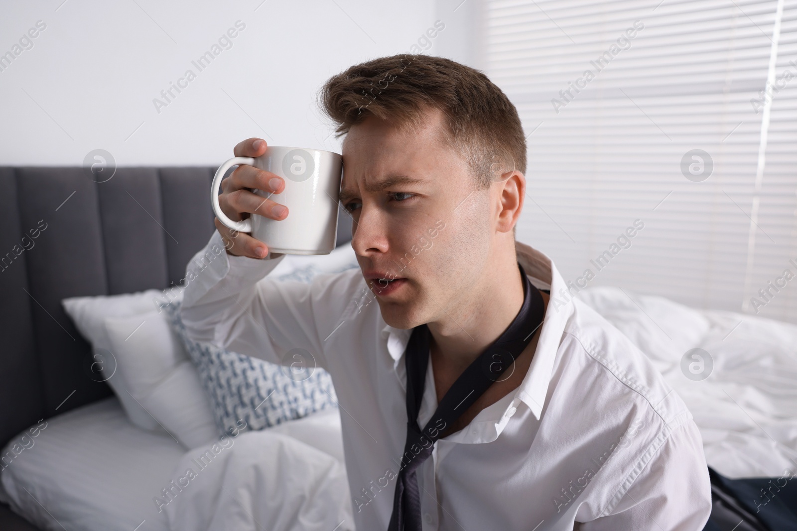 Photo of Sad young man with cup of coffee getting ready at home