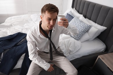 Photo of Sad young man with cup of coffee getting ready at home