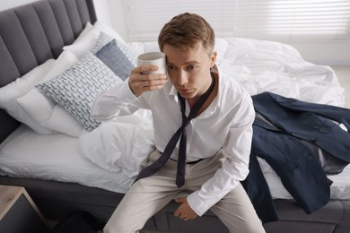 Photo of Sad young man with cup of coffee getting ready at home