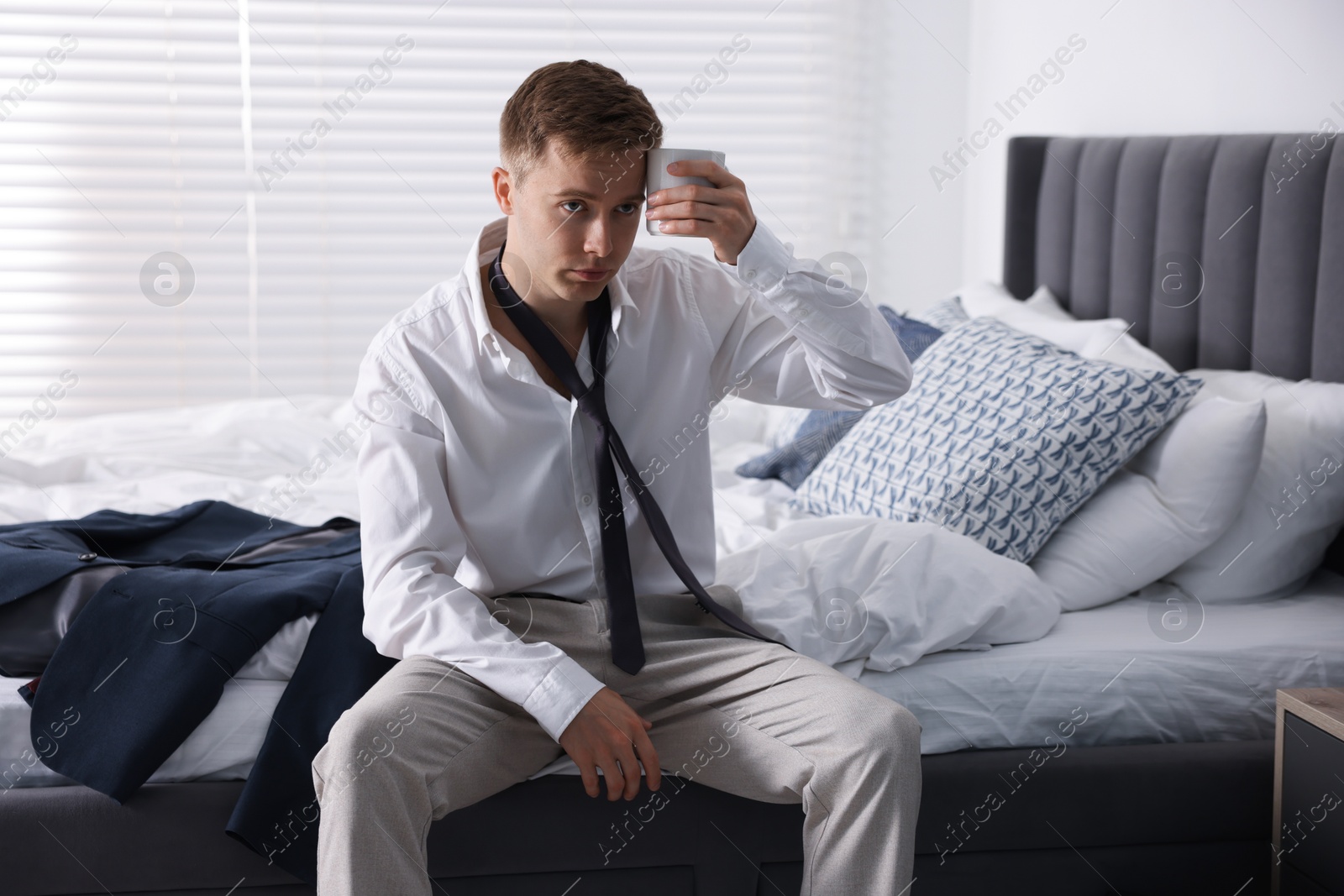 Photo of Sad young man with cup of coffee getting ready at home