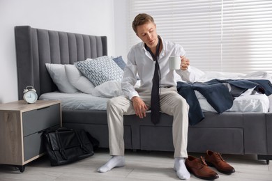 Photo of Sad young man with cup of coffee getting ready at home