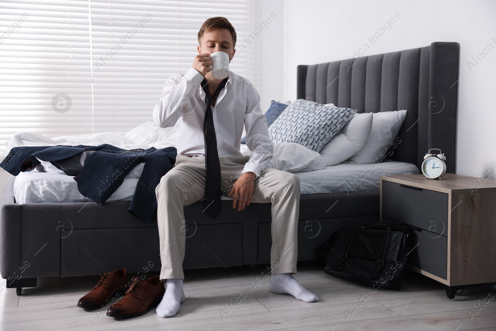 Photo of Sad young man with cup of coffee getting ready at home