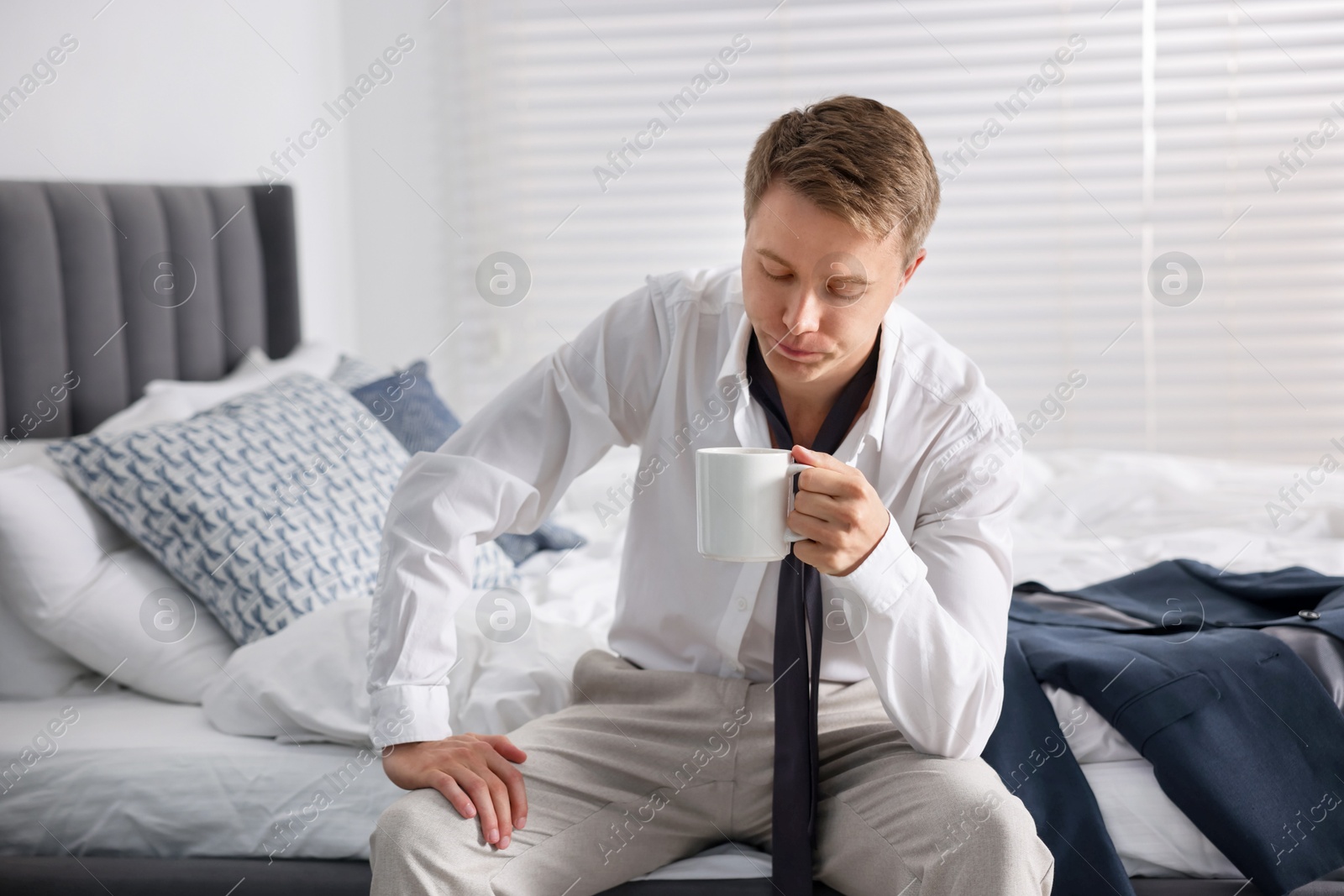 Photo of Sad young man with cup of coffee getting ready at home